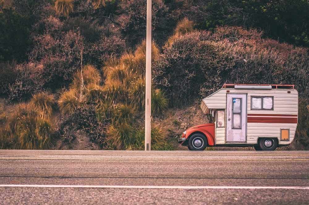 Camper blanc et rouge stationné sur le bord de la route, près de buissons et d'un mât de ligne