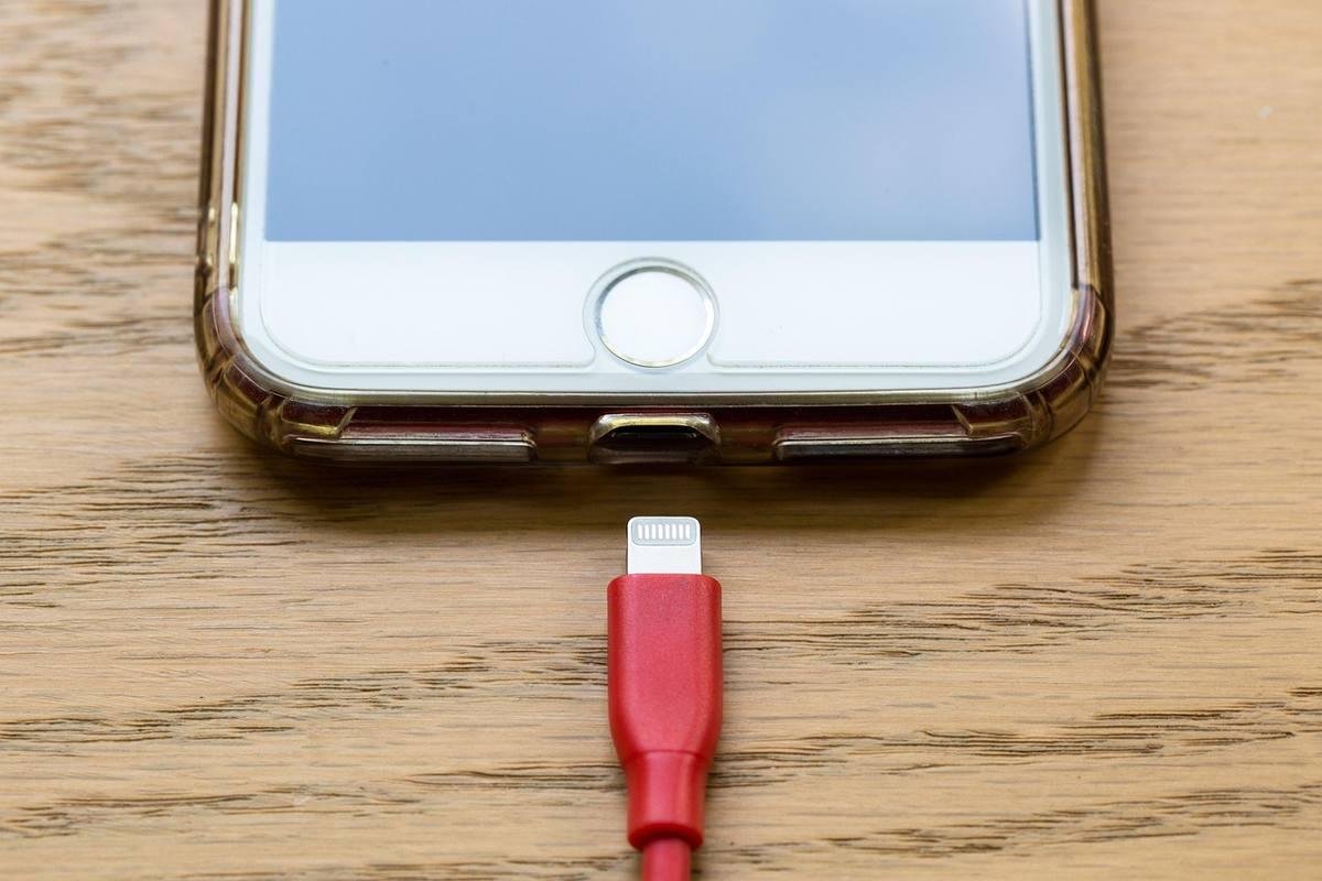 Smartphone connecté à un câble rouge sur une surface en bois