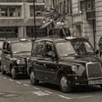 Des taxis noirs en rangée sur une rue de ville, piéton à droite