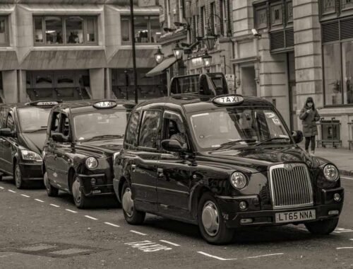 Des taxis noirs en rangée sur une rue de ville, piéton à droite