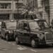 Des taxis noirs en rangée sur une rue de ville, piéton à droite