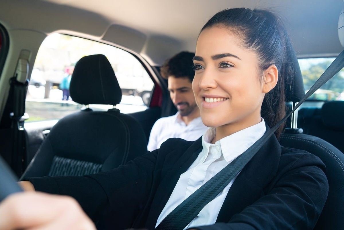 Une femme souriante conduit une voiture avec un passager à l'arrière