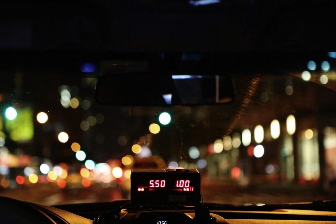 Compteur de taxi illuminé affichant le tarif nocturne sur une route urbaine avec bokeh lumineux