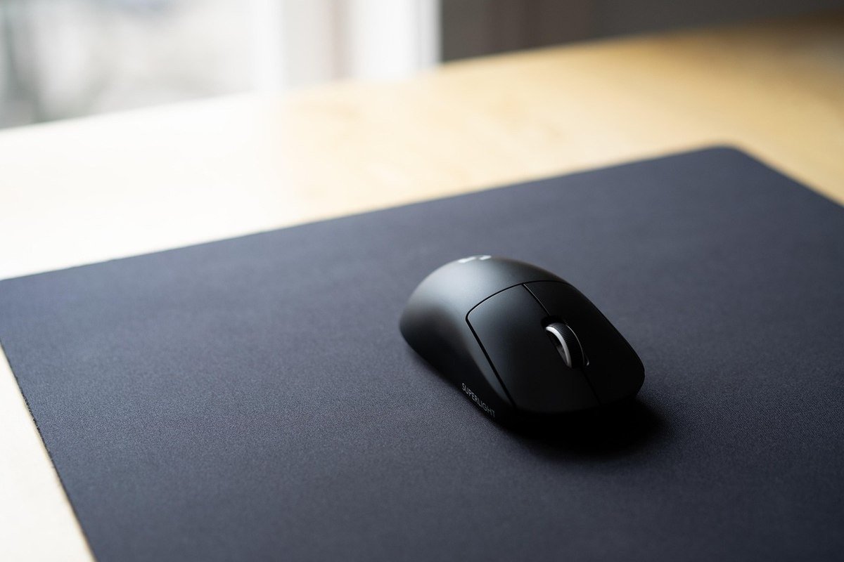 Souris noire sur tapis gris foncé, lumière douce, bureau en bois clair