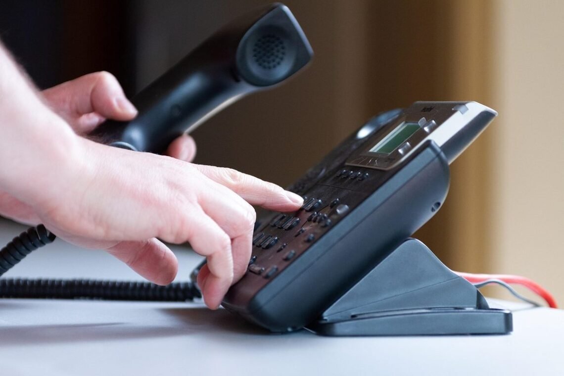 Une main appuie sur les touches d'un téléphone de bureau