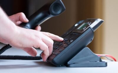 Une main appuie sur les touches d'un téléphone de bureau