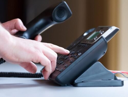 Une main appuie sur les touches d'un téléphone de bureau