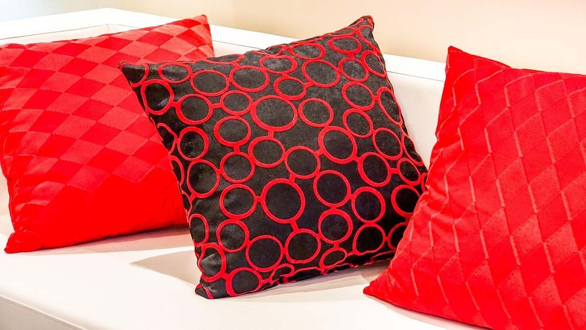 Trois coussins rouges et noirs aux motifs géométriques sur un canapé blanc