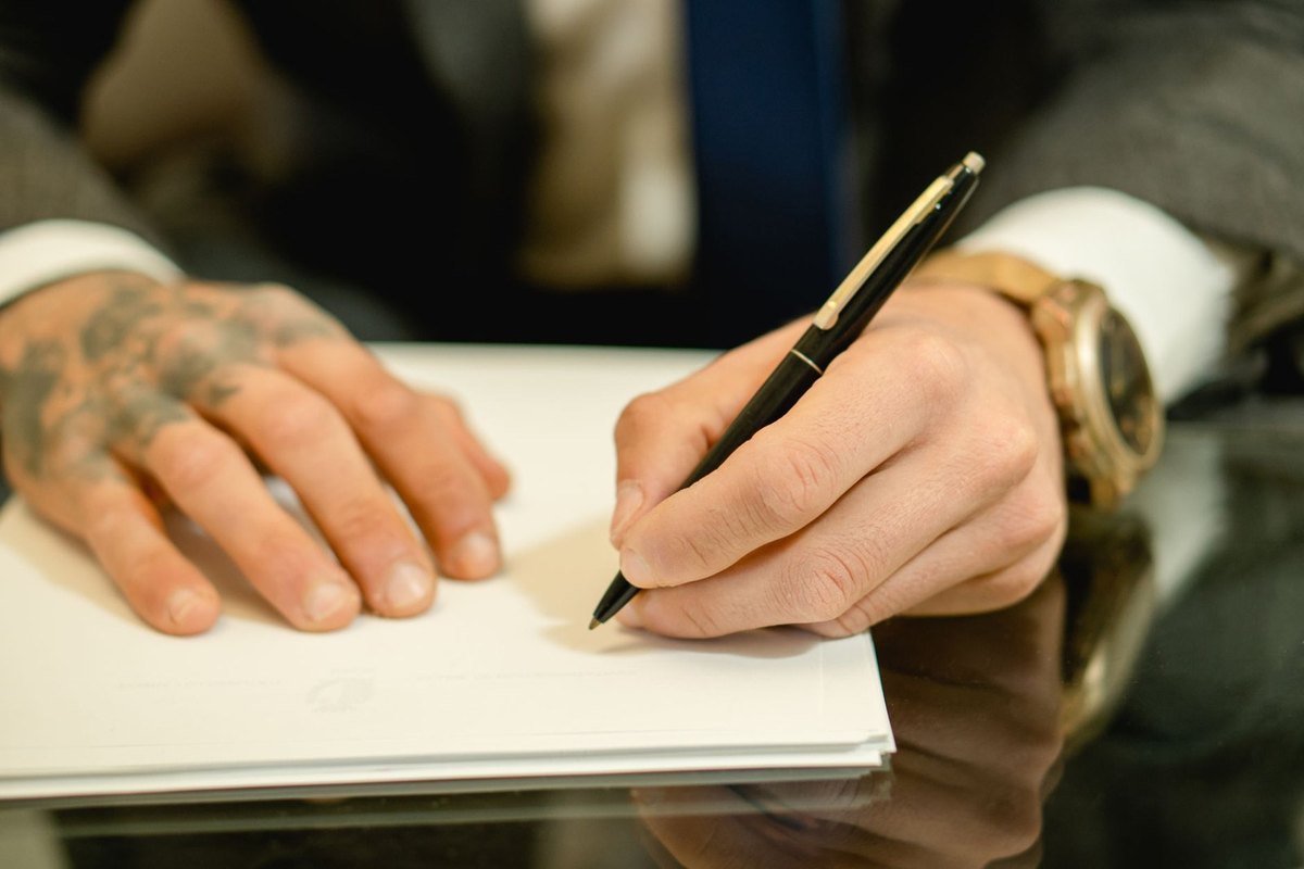Mains tatouées écrivant sur un papier avec un stylo noir