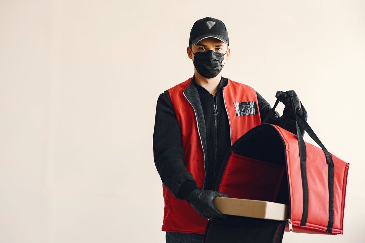 Livreur avec un sac rouge et un colis, en noir et rouge, contre fond neutre
