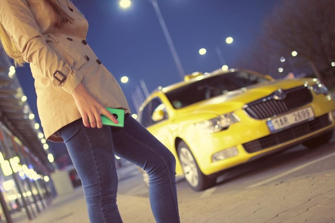 Femme tenant un téléphone vert la nuit devant un taxi jaune