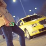 Femme tenant un téléphone vert la nuit devant un taxi jaune