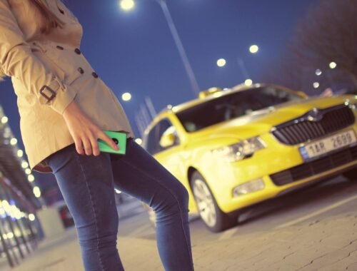 Femme tenant un téléphone vert la nuit devant un taxi jaune