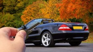 Une main tenant des clés devant une voiture cabriolet noire sur route