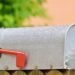 Boîte aux lettres métallique sur clôture en bois, fleur orange à droite