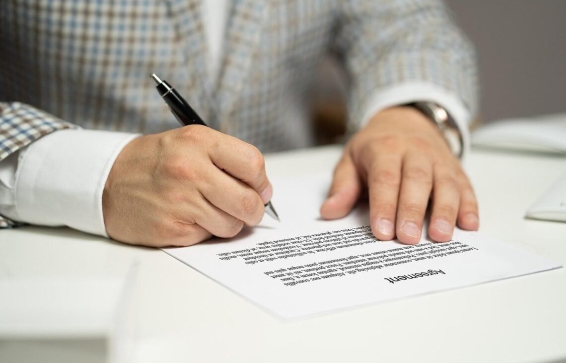 Homme écrivant sur un document avec un stylo noir à la table