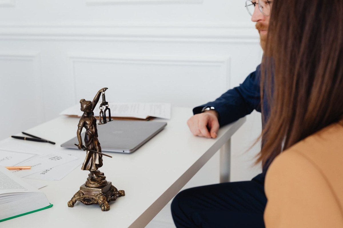Table blanche avec statue de justice, ordinateur et papiers, deux personnes en conversation