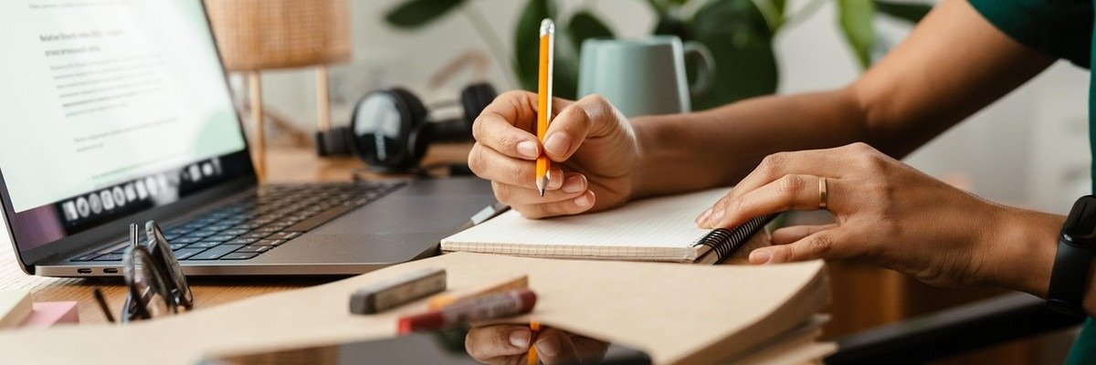 Person écrivant dans un carnet à côté d'un ordinateur portable et d'un smartphone