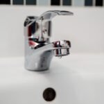 Robinet d'évier en chrome avec goutte d'eau, carrelage blanc, trou d'écoulement