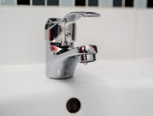 Robinet d'évier en chrome avec goutte d'eau, carrelage blanc, trou d'écoulement