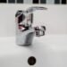 Robinet d'évier en chrome avec goutte d'eau, carrelage blanc, trou d'écoulement
